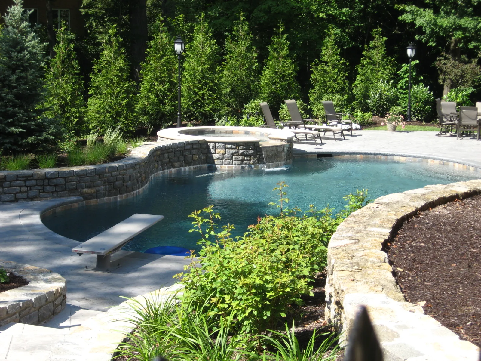 Freeform pool and raised spa framed by curved stone walls