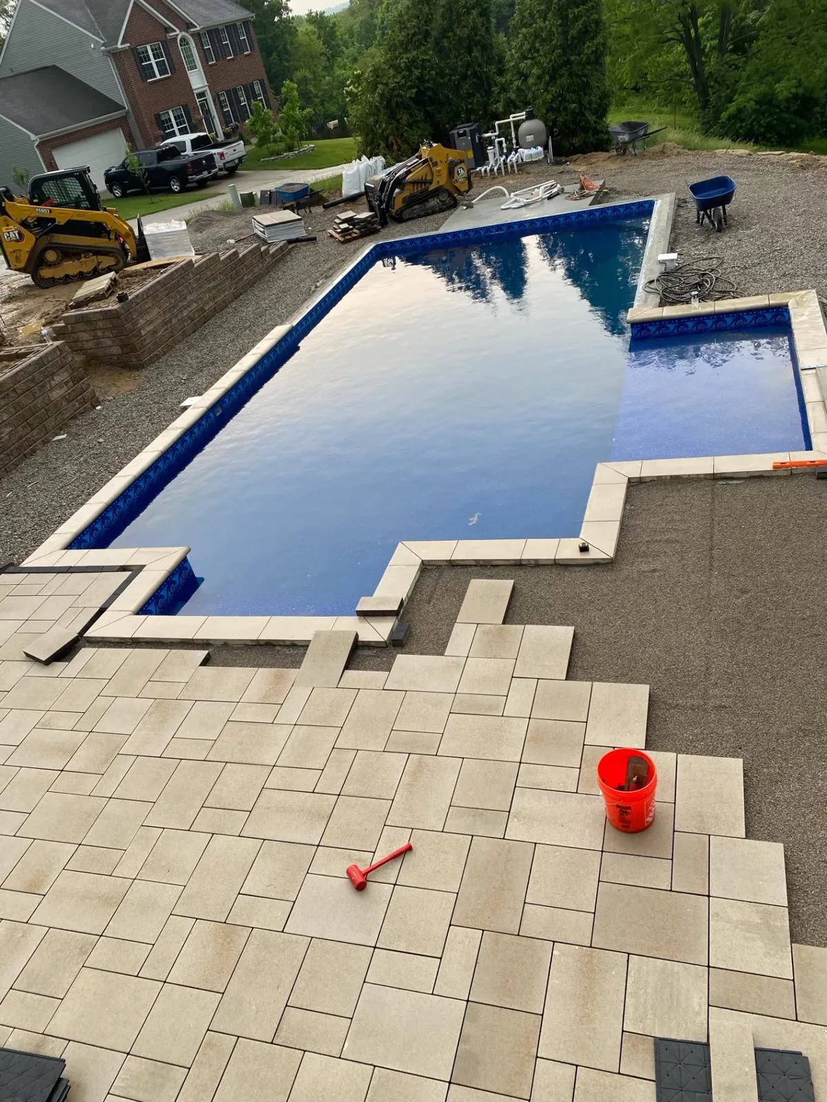 Patterned paver deck being laid around a pool beside retaining wall construction