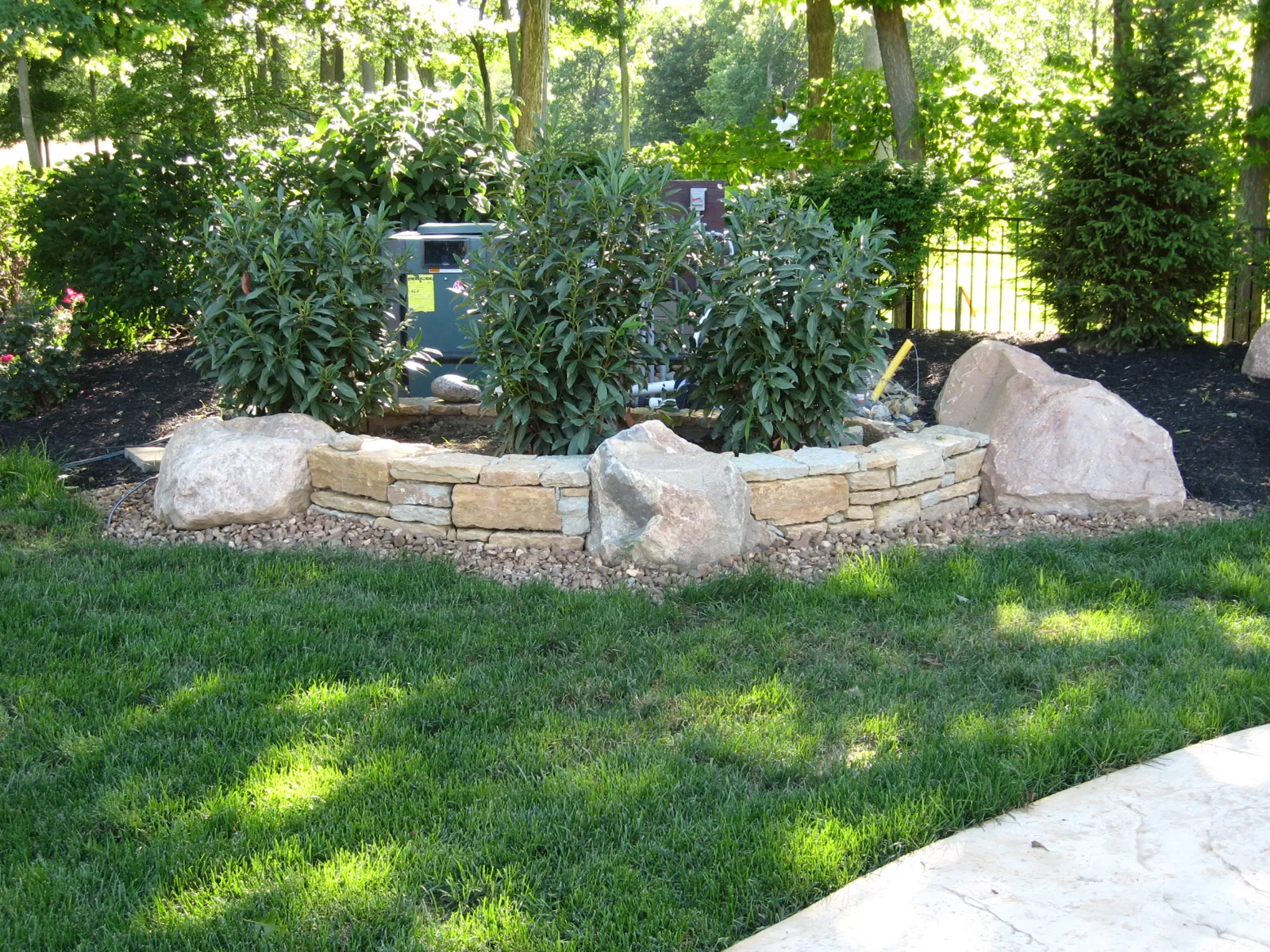 Limestone planter with boulders and evergreens beside the pool
