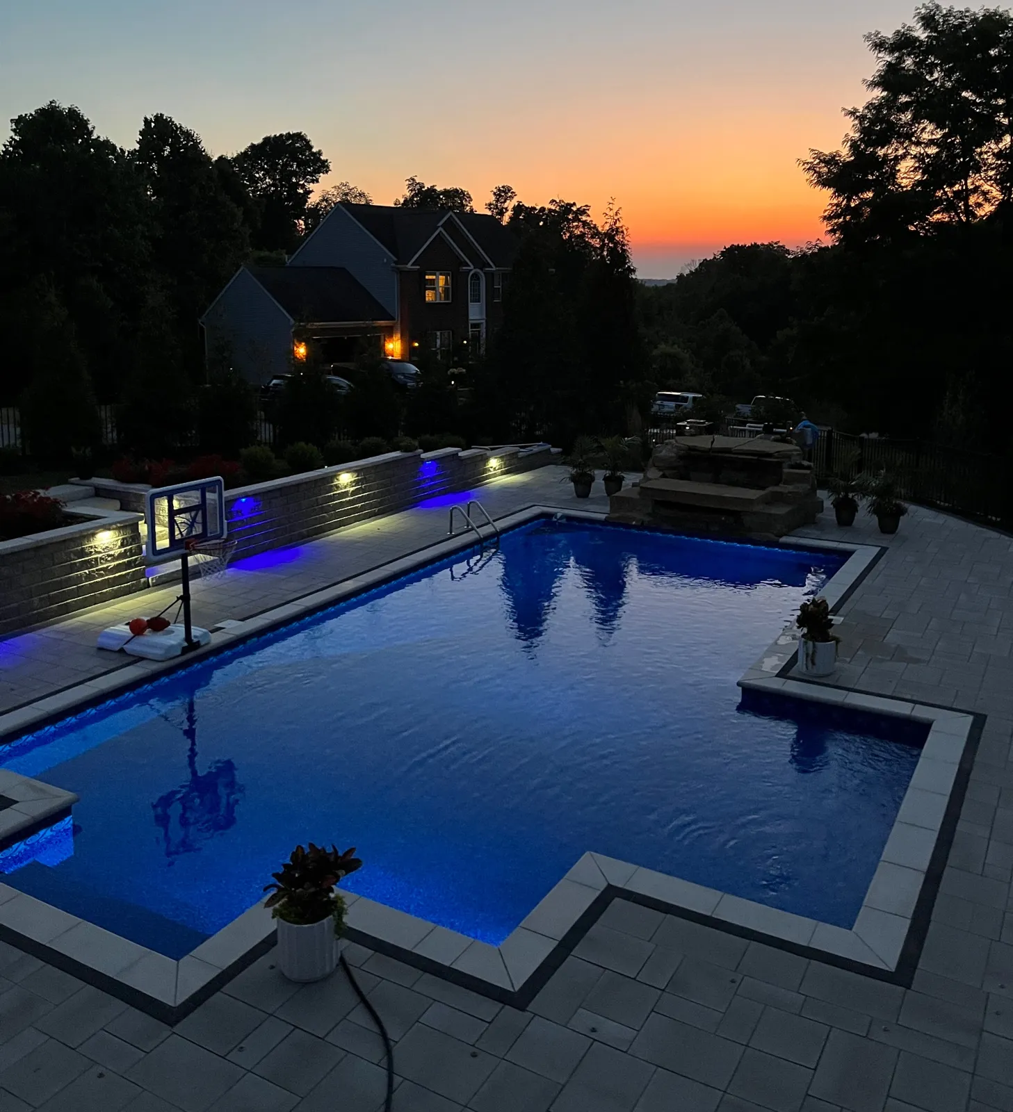 Finished pool glowing blue at dusk with illuminated stone retaining walls