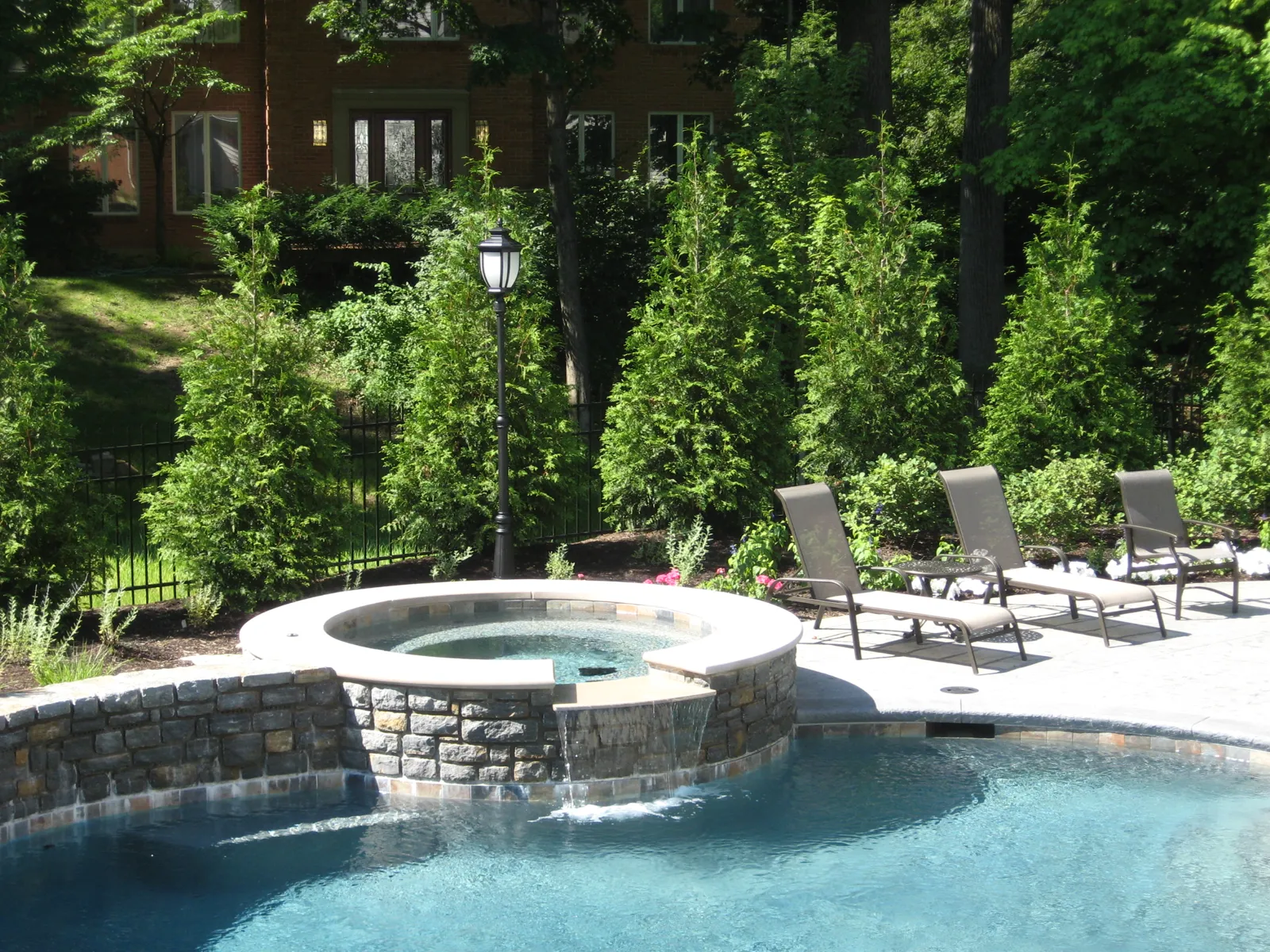 Stone-faced raised spa spilling into the pool with privacy evergreens