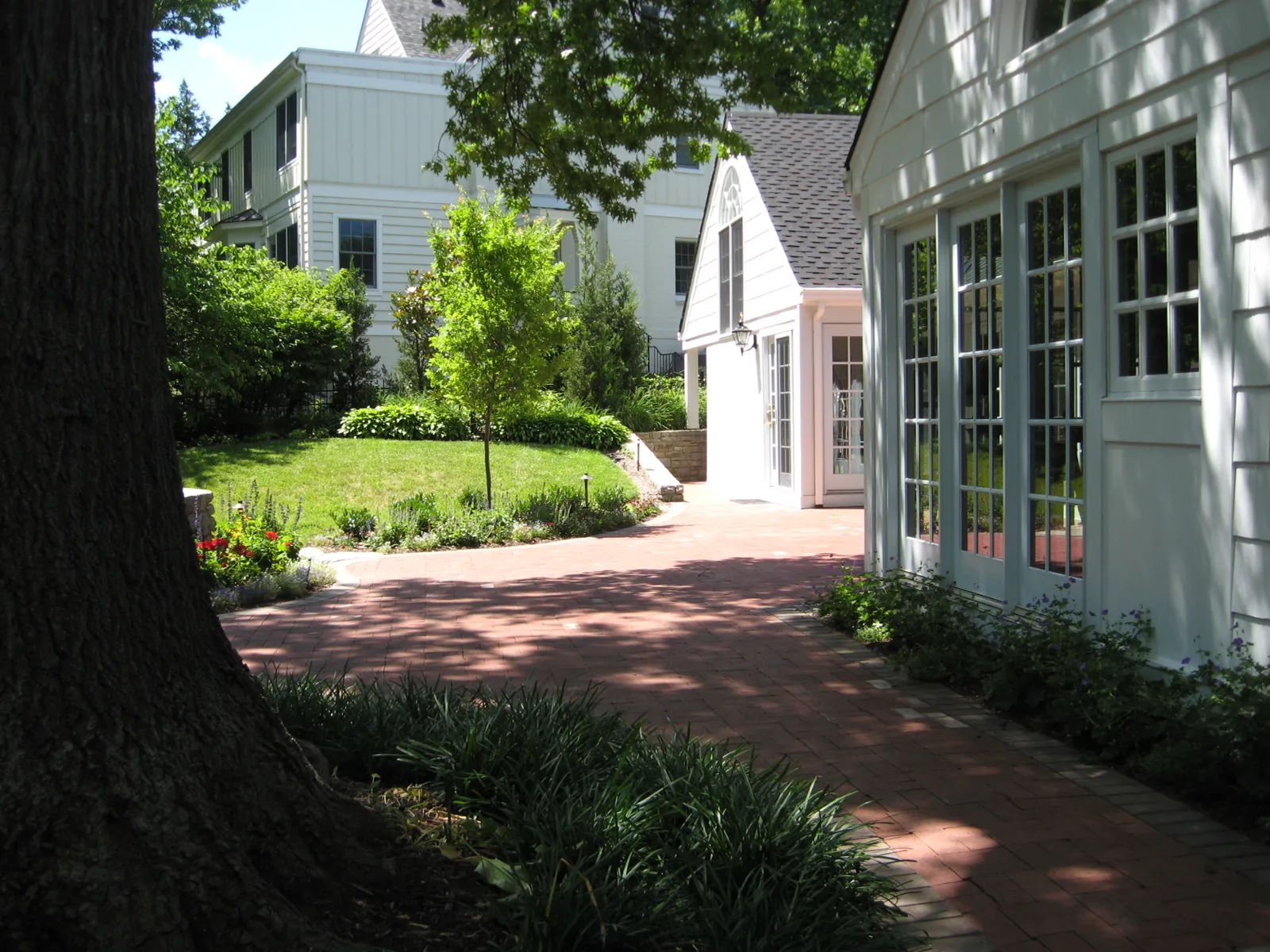 Curving brick paver walk along the house under mature shade trees