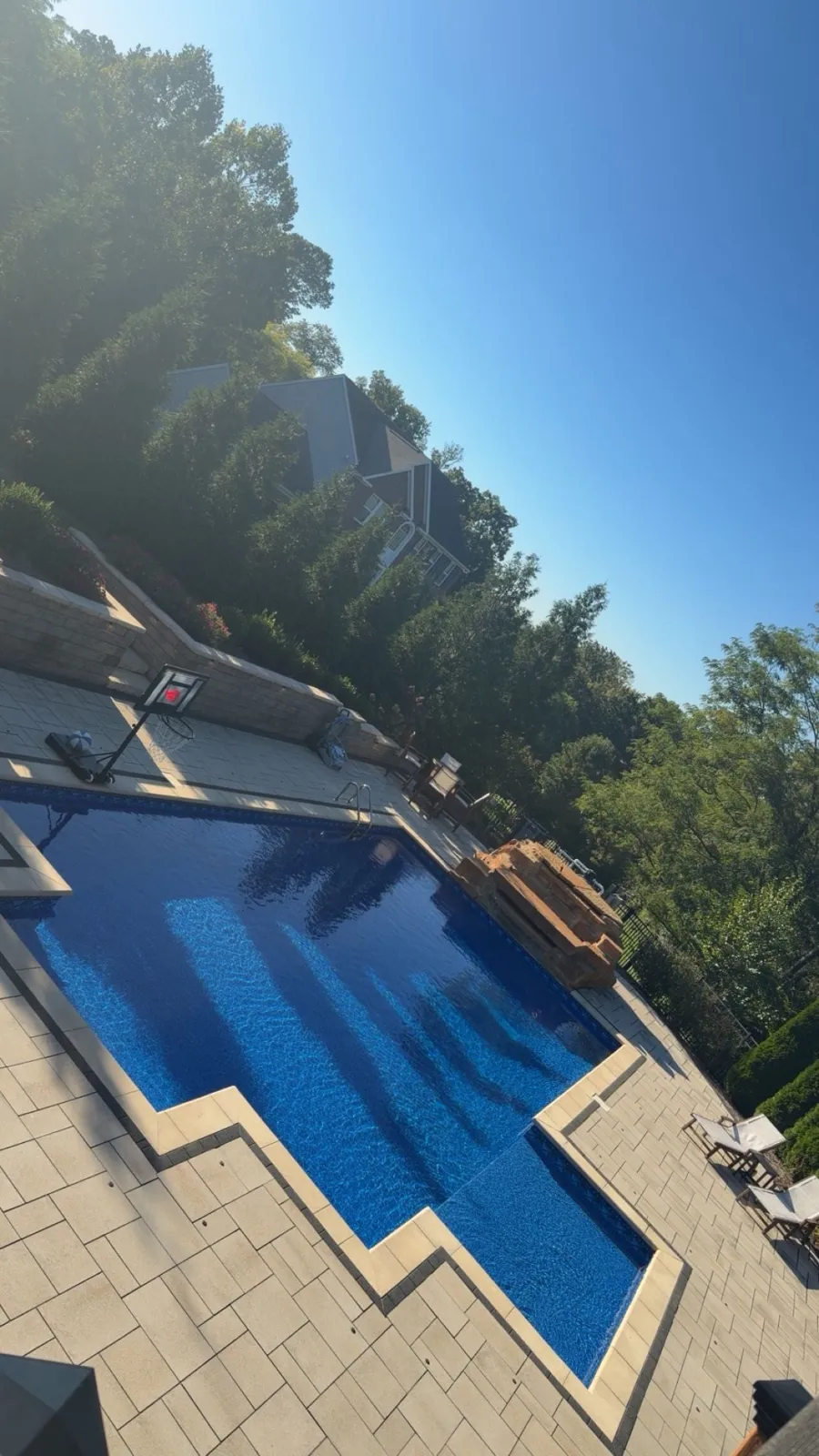 Angled aerial of an L-shaped pool with paver decking and retaining walls