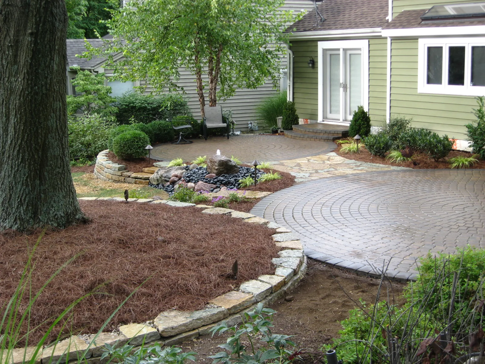 Twin circular paver patios joined by flagstone with a bubbling rock fountain