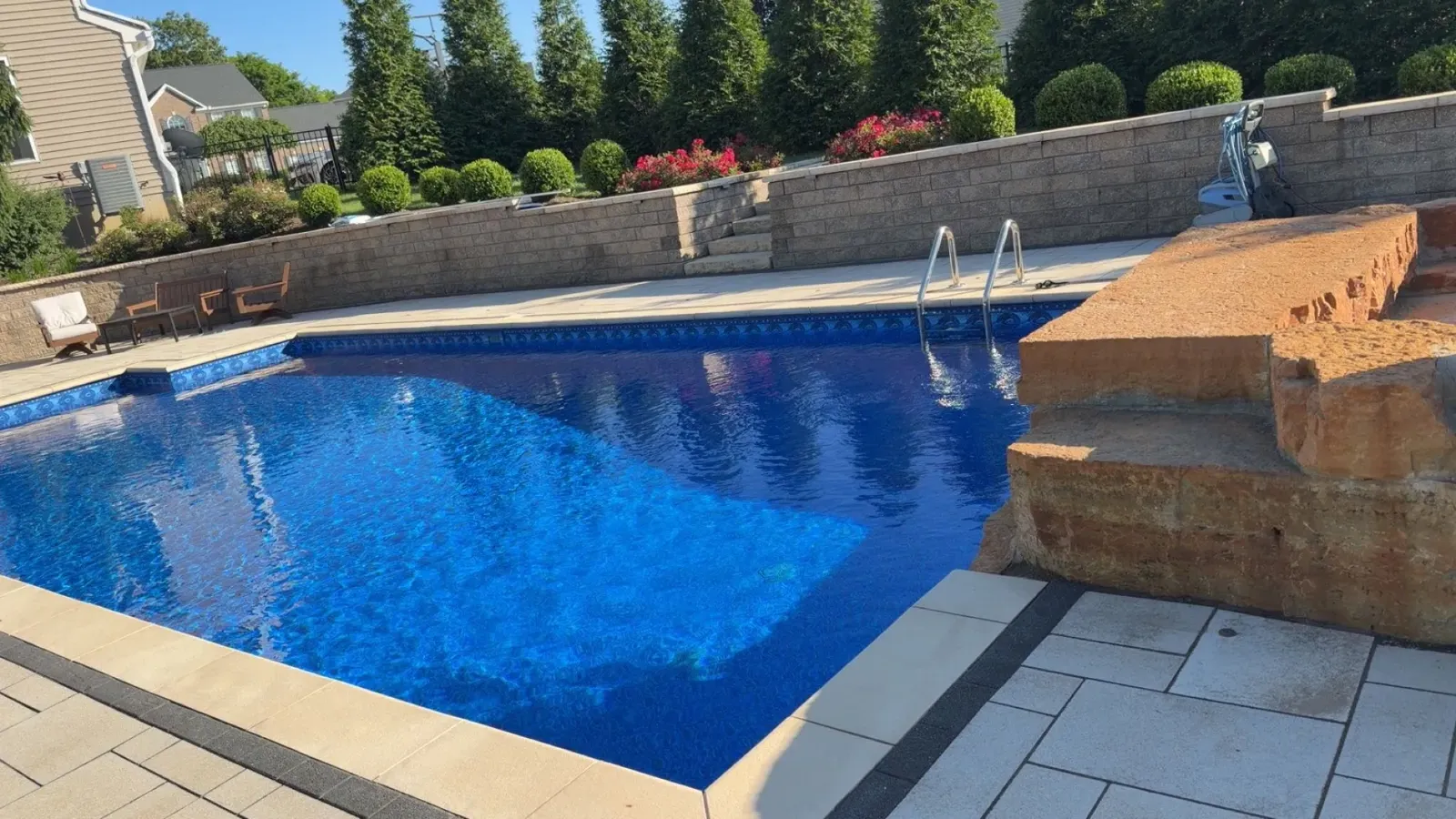 Blue pool beside a natural stone waterfall and paver deck