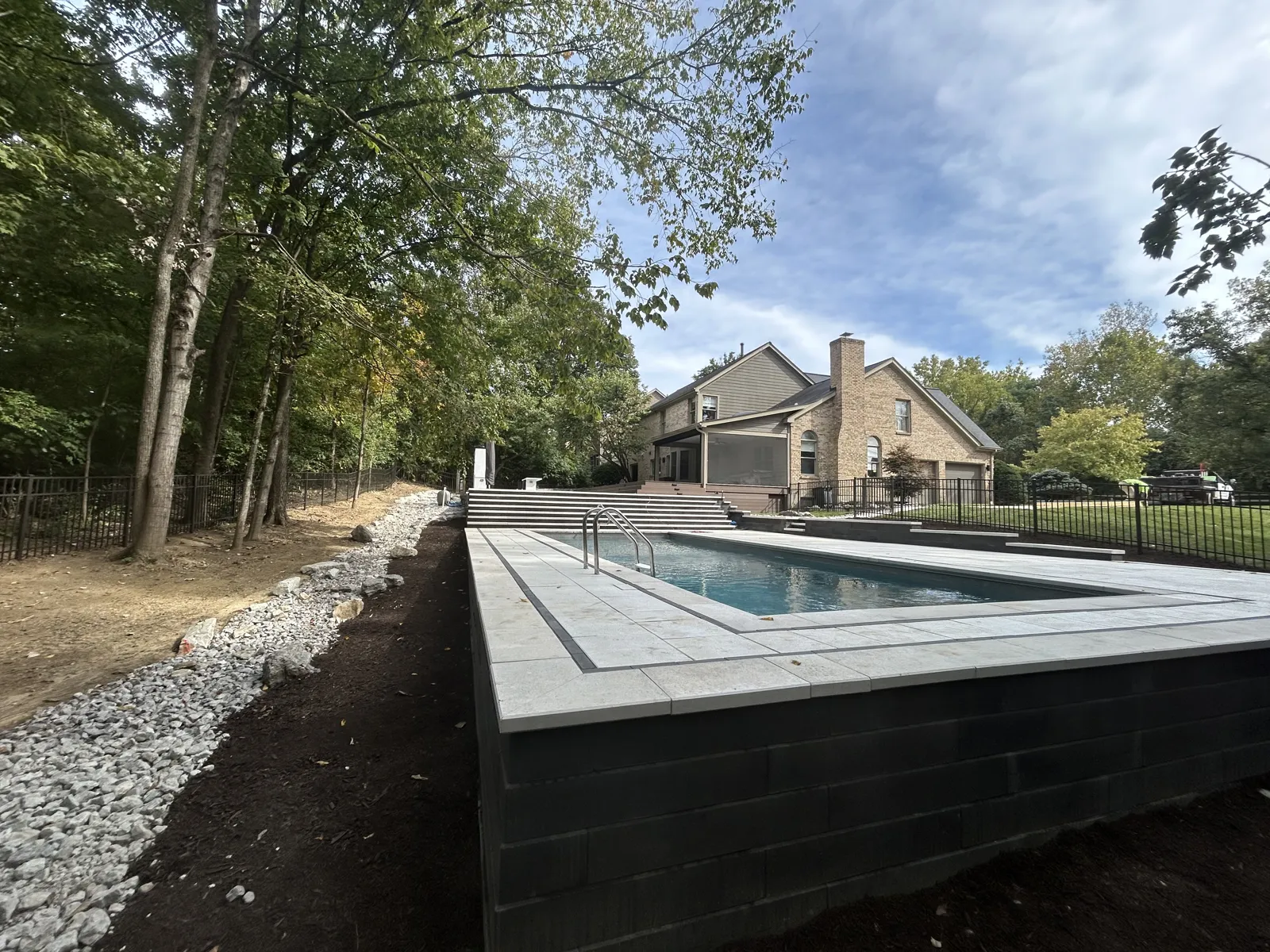 Pool deck elevated on a dark retaining wall above freshly graded lawn