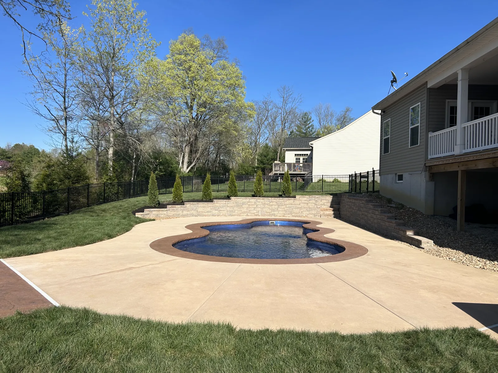 Freeform pool with a wide concrete patio and new lawn