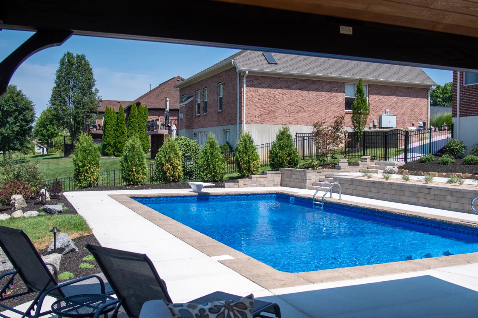 Tiered retaining walls, lawn and planting beds connecting a pool to a custom timber pavilion